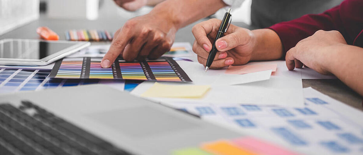 Teamarbeit kreativer Designer, die an neuen Projekten arbeiten und Farbmuster für die Auswahlfärbung auf einem digitalen Grafiktablett mit Arbeitswerkzeugen und -ausrüstung am Arbeitsplatz auswählen.